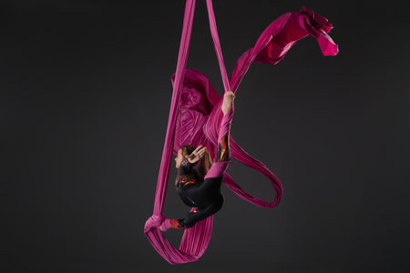 Girl performs aerial silk stunt with pink fabric in studio settingの写真素材