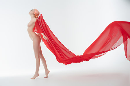 Woman in elegant pose with flowing red fabric in a minimalist studio settingの写真素材