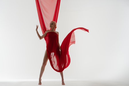 Elegant woman poses in vibrant red fabric against a light backdropの写真素材