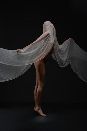 Red woman striking an artistic nude pose with flowing fabric in dark settingの写真素材