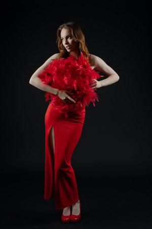 Elegant woman in stunning red dress holding vibrant feathers while posing in studio setting with emotional expressionの写真素材