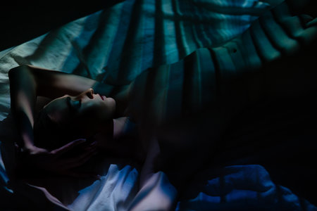 Woman relaxed on bed, shadows and light from projector creating artistic effectsの写真素材