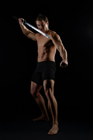 Strong man performing a dynamic sword technique indoors in low light settingの写真素材