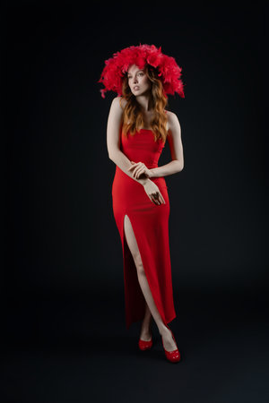 Woman posing with emotion in a studio setting, wearing a striking red dress and a bold feathered headpieceの写真素材