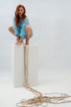Red-haired woman poses elegantly with rope on a white backdropの写真素材