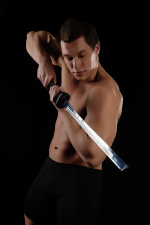 Dynamic pose of a muscular man wielding a sword in artistic lighting setupの写真素材