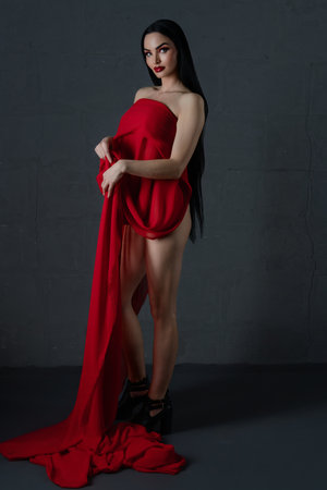 Elegant woman in stylish lingerie draped with luxurious red fabric indoorsの写真素材