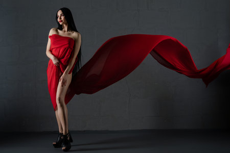 Elegant woman draped in flowing red fabric accentuates beauty and allureの写真素材