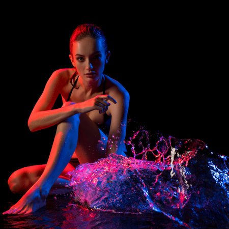 Model interacts with vibrant water splashes in creative lighting setupの写真素材