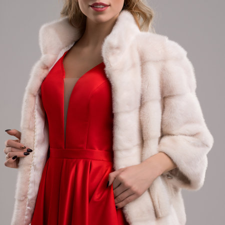 Elegant woman wearing a red dress and fur coat in a studio settingの写真素材
