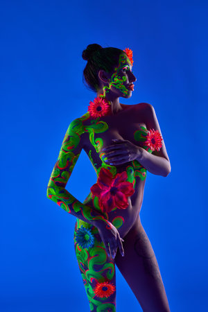 Woman with fluorescent body art covering naked breast against blue backgroundの写真素材