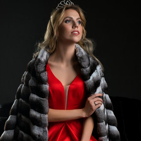 Elegant young woman in a red gown, fur shawl, and tiaraの写真素材