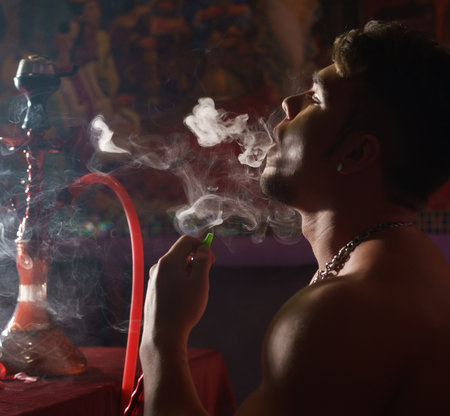 Young athletic tattooed man smoking hookah
