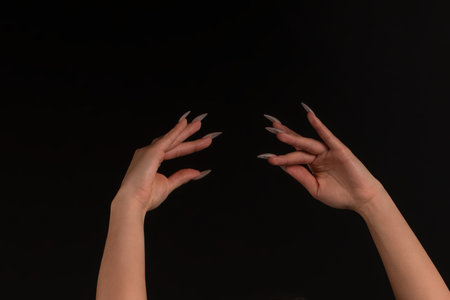 Two arms with long nails reaching on black backgroundの写真素材