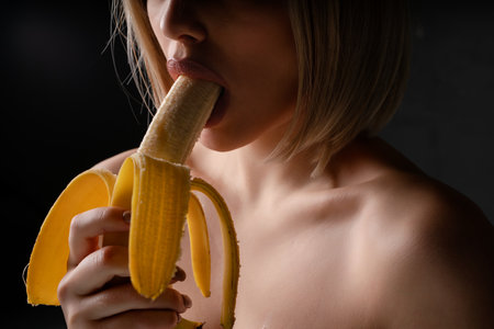 Woman enjoying a banana in a sensual pose under soft lightingの写真素材