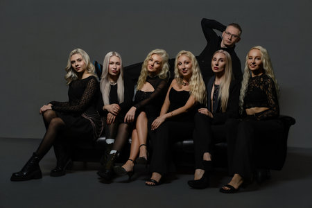 Group of seven people in stylish black outfits posing together in a modern studio settingの写真素材