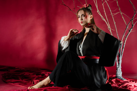 Woman in traditional Japanese dress poses elegantly in a studio setting with a vibrant red backdropの写真素材