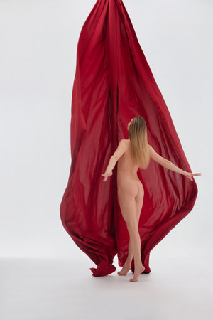 Model poses gracefully behind flowing red fabric in a studio settingの写真素材