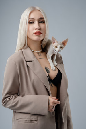 A stylish woman poses confidently with her cat on her shoulder in a studioの写真素材