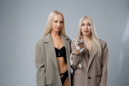Two women in stylish blazers hold a cat in a modern studio settingの写真素材