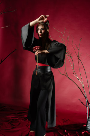 Woman poses gracefully in traditional dress in a studio with a red backdropの写真素材