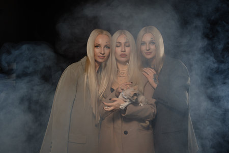 Three women with long blonde hair pose together in a smoky atmosphere at nightの写真素材