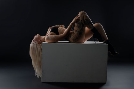 Model poses gracefully on a large cube in a dark studio settingの写真素材