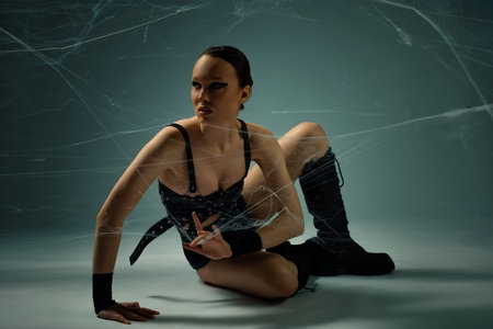 Woman in black gothic attire posing dynamically while tangled in spiderwebs.の写真素材