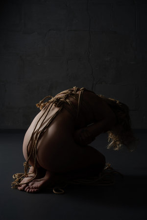 Shibari art with a naked woman in a dimly lit roomの写真素材