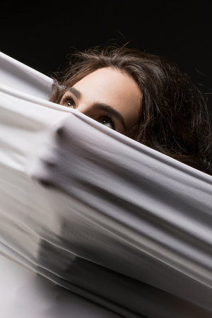Womans face peeks over white fabric against black backgroundの写真素材