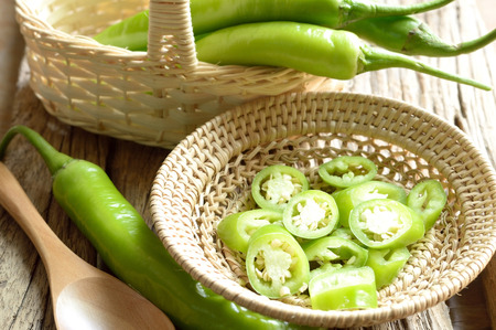 green pepper in wicker basket on wooden backgroundの写真素材