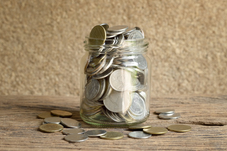 side view of coins in glass bottle on wooden background, thai baht