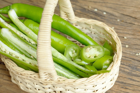 green pepper in wicker basket on wooden backgroundの写真素材