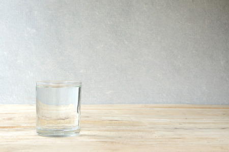 glass of purified water on wooden table - concrete wall background