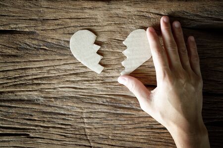 woman hand holding broken heart paper cut on wooden background - love concept