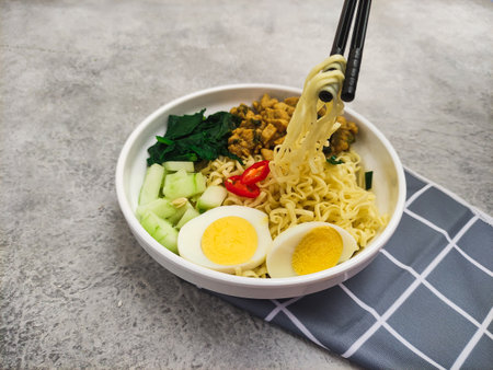 Using chopsticks take a delicious noodles. Noodle with chicken cubes, egg sliced and vegetable in a bowl.の写真素材
