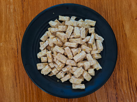 Raw tempeh cut placed on black plate with wooden background. Ready to cookの写真素材