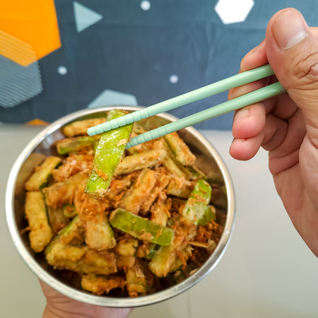 The golden-brown of crispy fried eggplants slice with coconut grated, placed in a plate with chopsticks, held by handの写真素材
