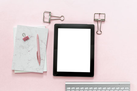 Desktop flat lay of office stationery items and blank tablet on pink backgroundの写真素材