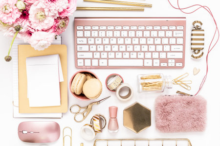 Feminine desktop with gold and pink stationery including a keyboard and mouseの写真素材
