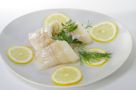fresh raw cod fish fillet on a plate with parsley and lemon