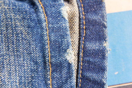 jeans stacked on a wooden background.Blue jeans on a brown wooden background.Frayed jeans.Detail of...