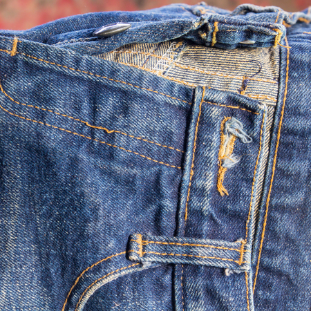 jeans stacked on a wooden background.Blue jeans on a brown wooden background.Frayed jeans.Detail of...