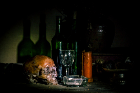 Human skull and candle with on wooden floor and old dirty wall background, and vase flower,and glass,and bottle of wine, still life concepの写真素材