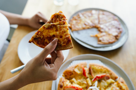 Woman taking slice of pizza from plate at table in restaurant, top viewの写真素材