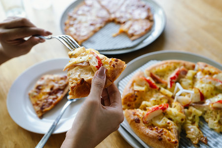 Woman eating pizza on wooden table. Close up of female hands holding fork and knife.