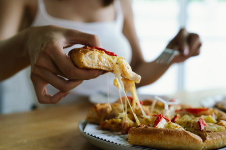 Pregnant woman eating pizza at home, closeup of handsの写真素材