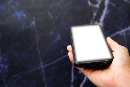 Smartphone with blank screen in hand on a dark marble background.