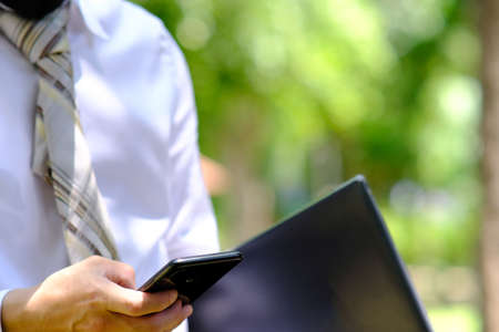Businessman using smart phone and laptop computer in the park with green background