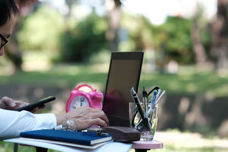 Close-up of business man using mobile phone and laptop computer in the park.の写真素材